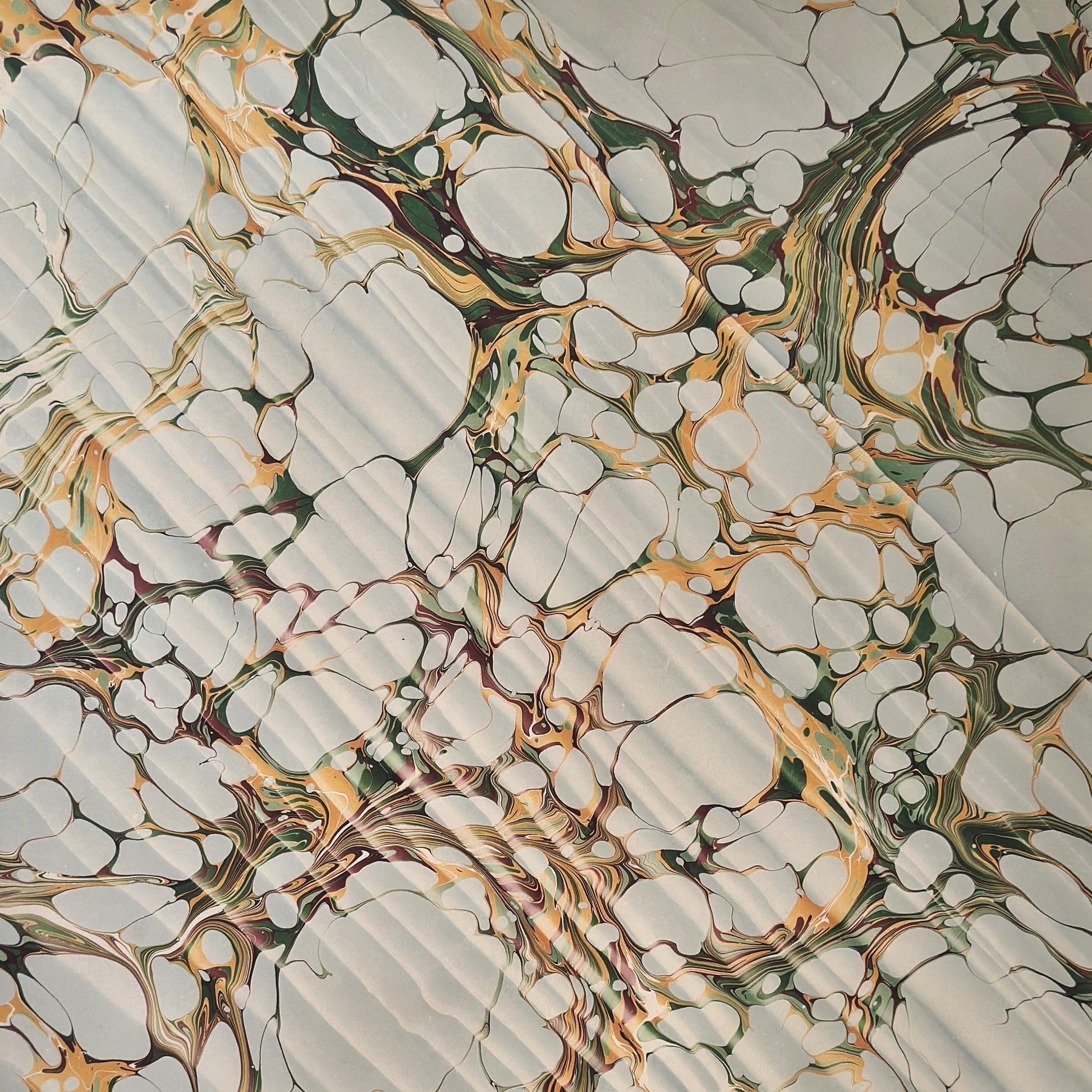 Printed marbled gift wrapping paper by Compton Marbling with a stone marbling pattern in soft grey, green and mustard.