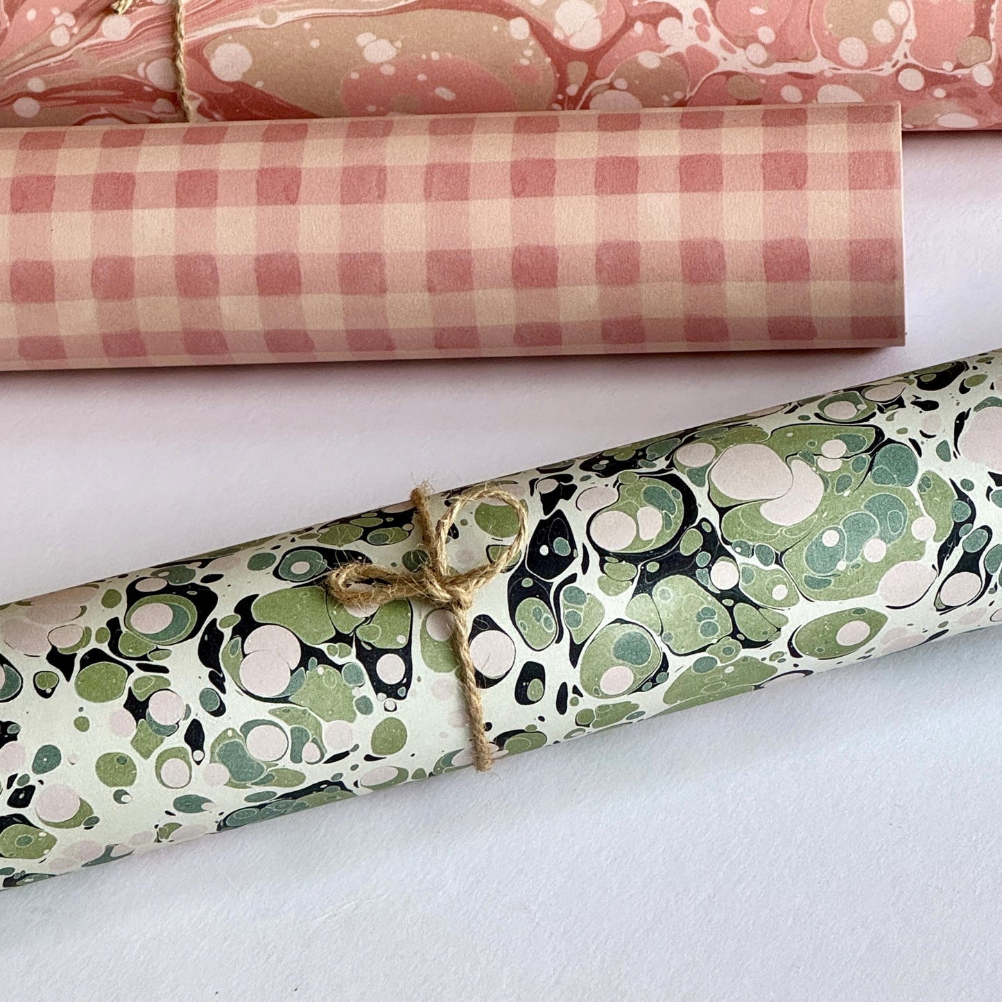 marbled printed wrapping paper with spot design in moss green, pale pink on a soft green. Pictured rolled alongside other papers