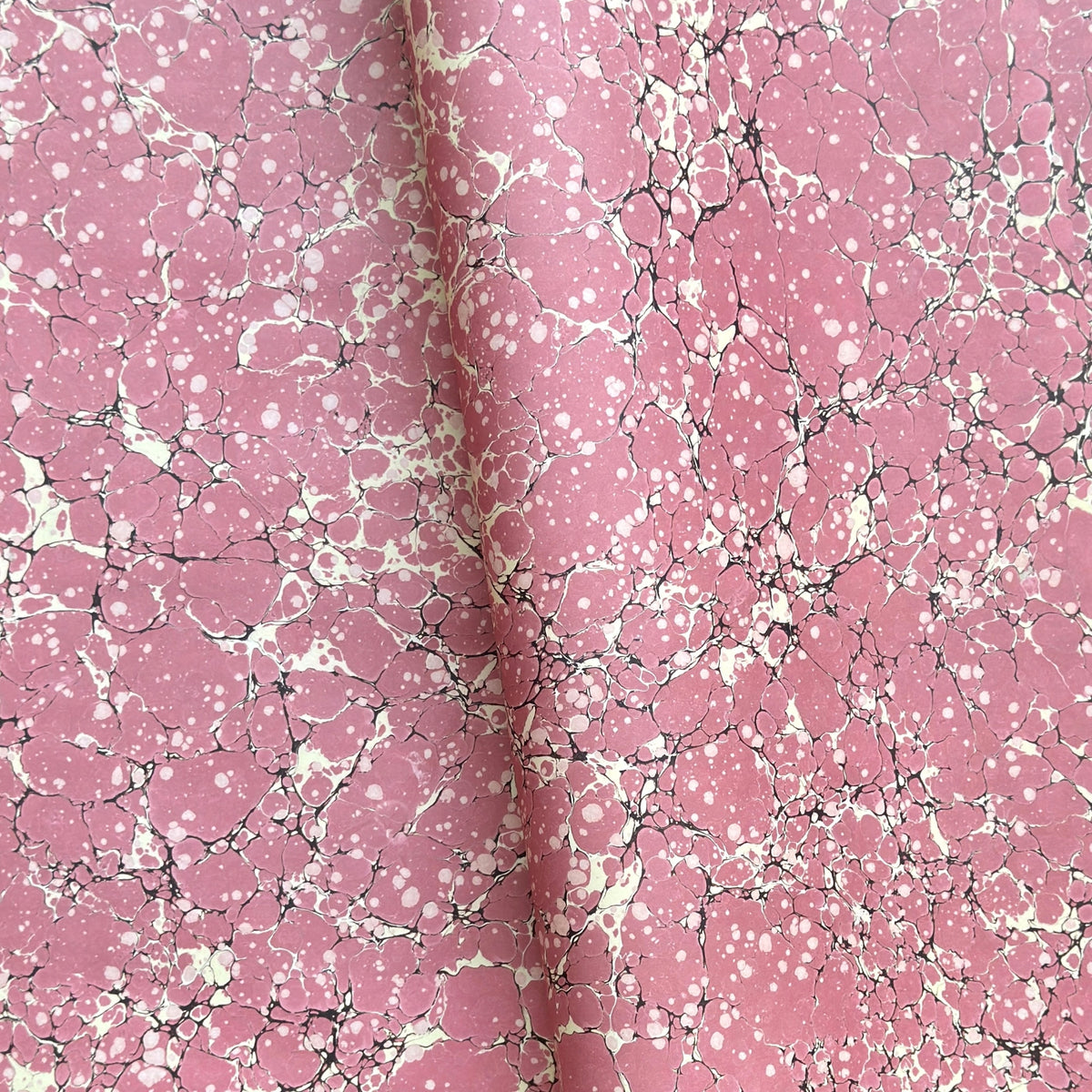 a sheet of wrapping paper with a pink marbled pattern with white and black veined design