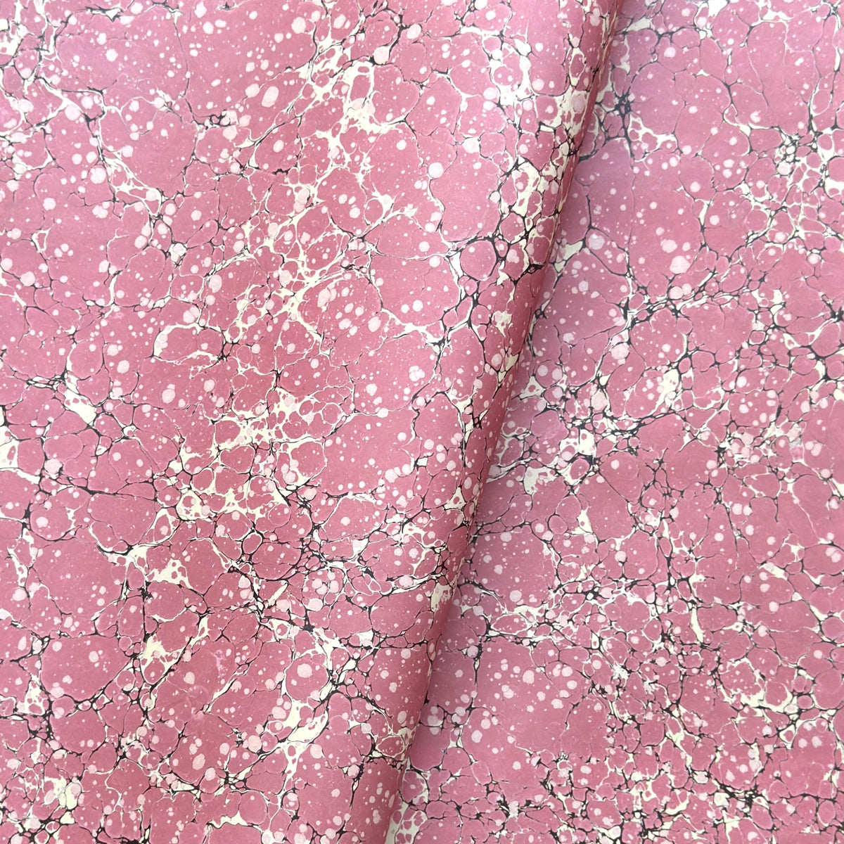 a sheet of wrapping paper with a pink marbled pattern with white and black veined design