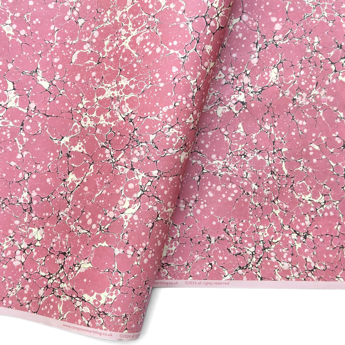a sheet of wrapping paper with a pink marbled pattern with white and black veined design