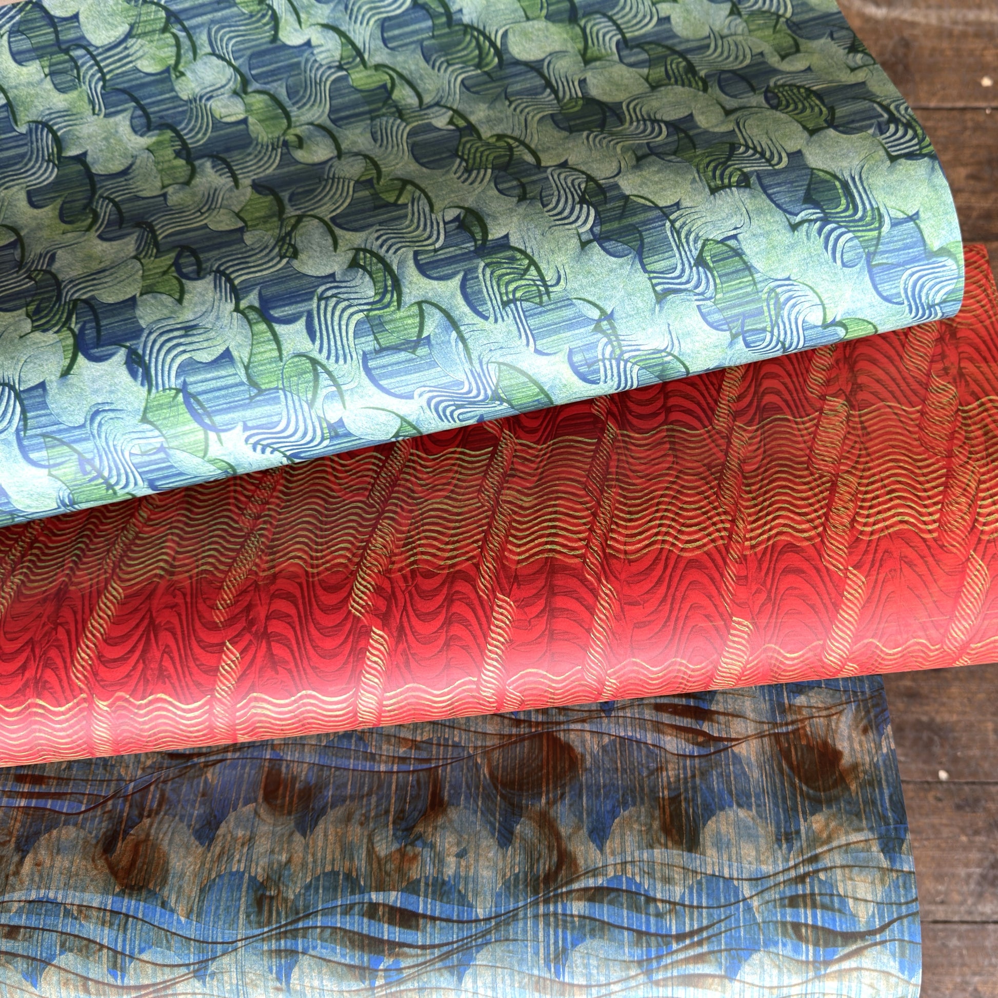 three sheets of wrapping paper with paste paper designs in greens, blue and reds
