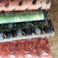 Four sheets of patterned paper stacked diagonally on a wooden floor. The fabrics feature traditional Japanese wave and floral motifs in various colors including pink, green, black, and rust red.