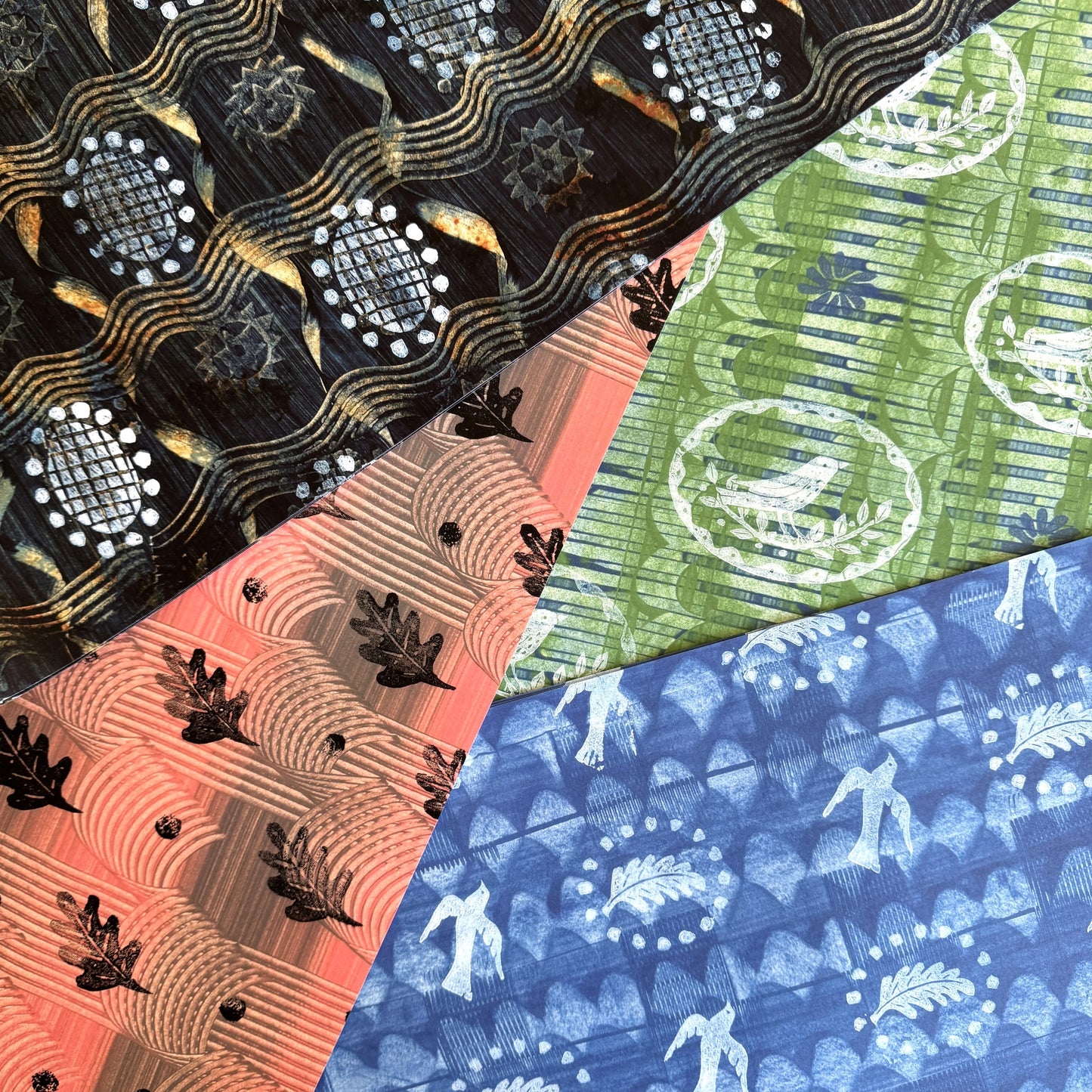  a sheet of wrapping paper with a relief printed black oak leaf on a coral pink paste paper backdrop. Pictured with other designs