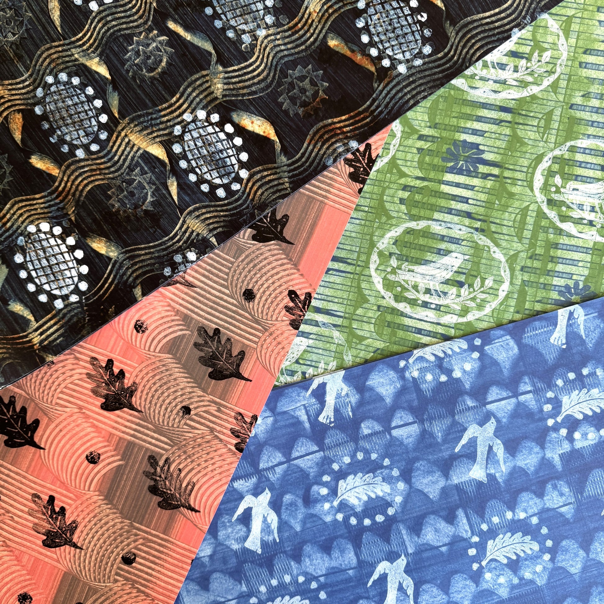  a sheet of wrapping paper with a relief printed black oak leaf on a coral pink paste paper backdrop. Pictured with other designs