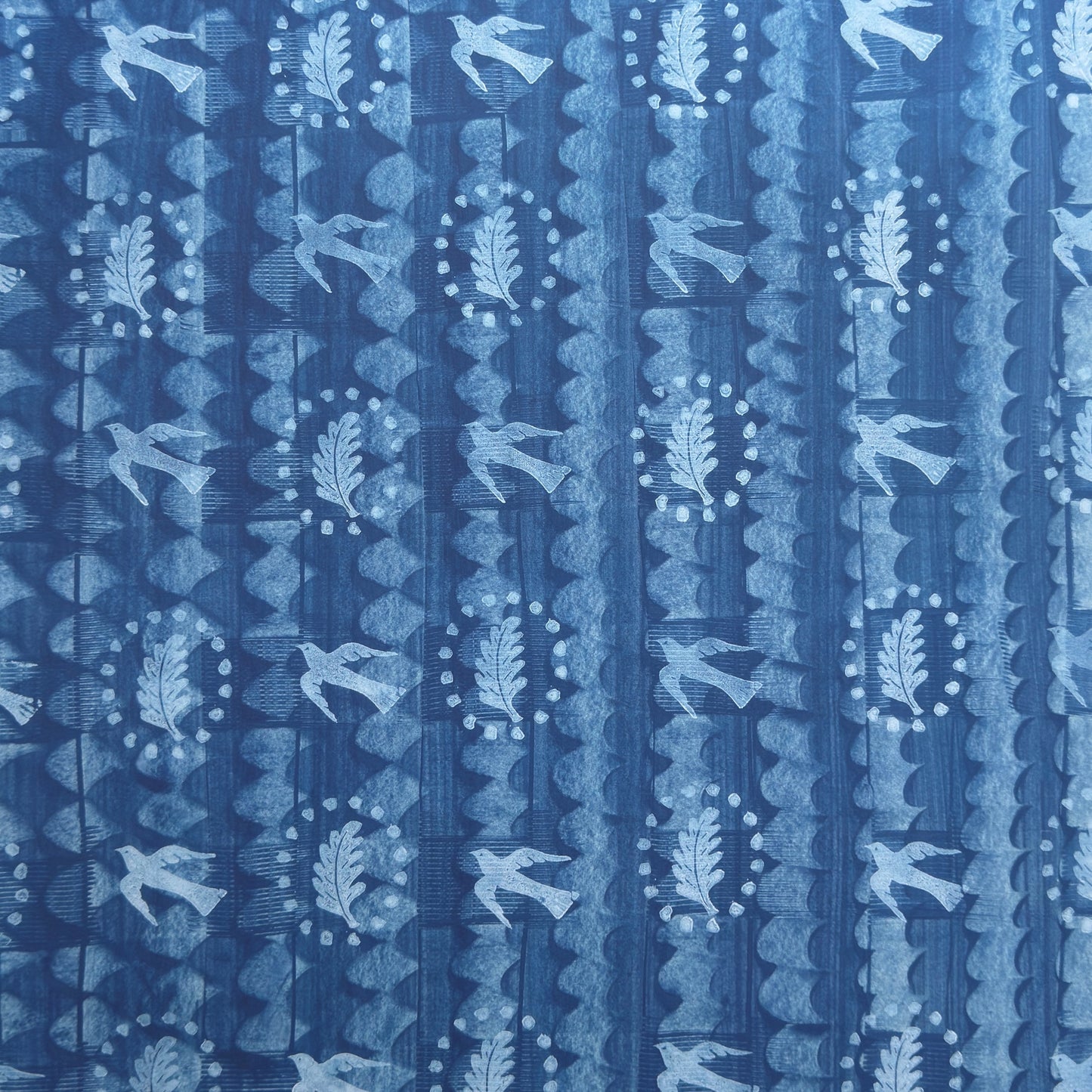 a sheet of wrapping paper with a relief printed oak leaf and bird in white on a blue paste paper backdrop
