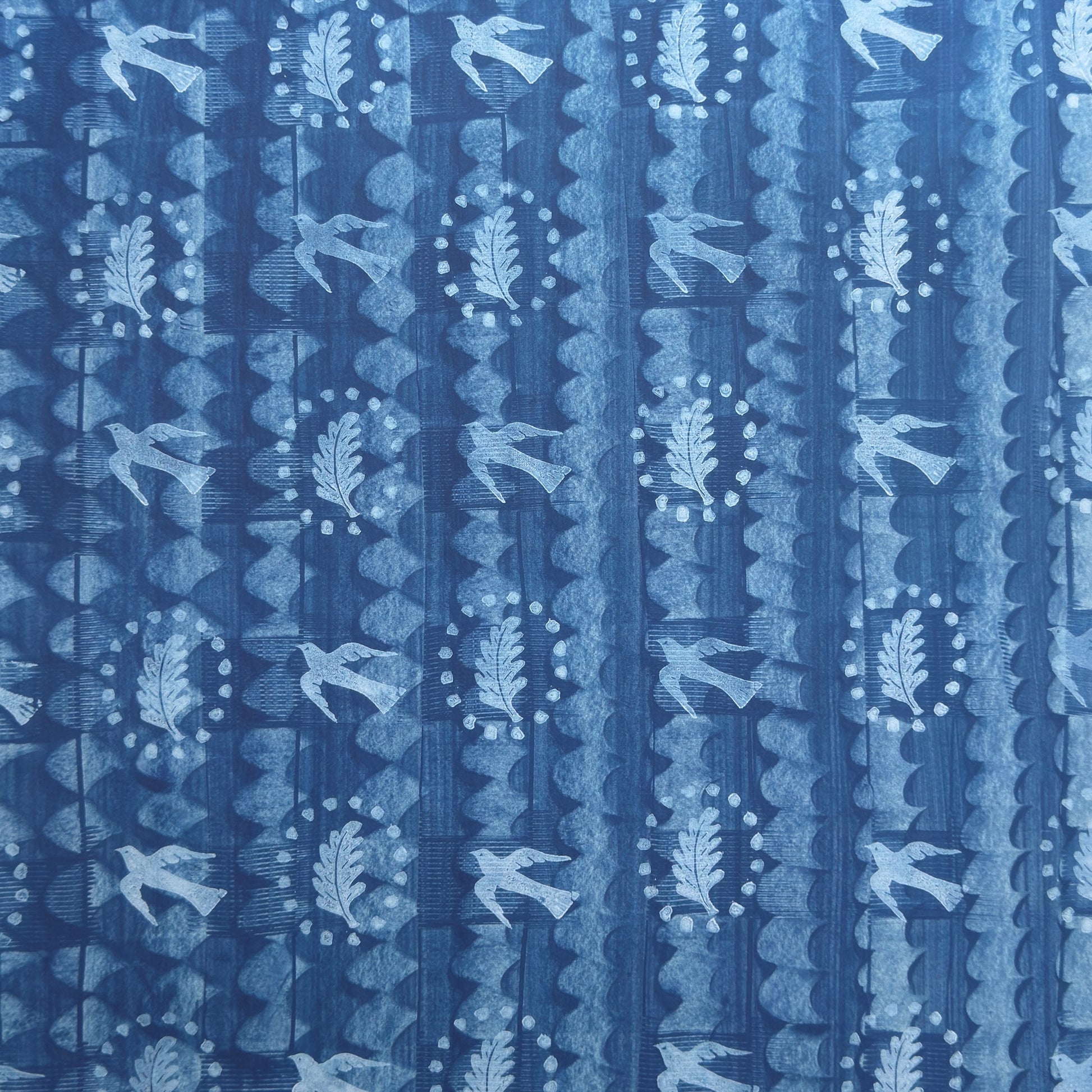 a sheet of wrapping paper with a relief printed oak leaf and bird in white on a blue paste paper backdrop