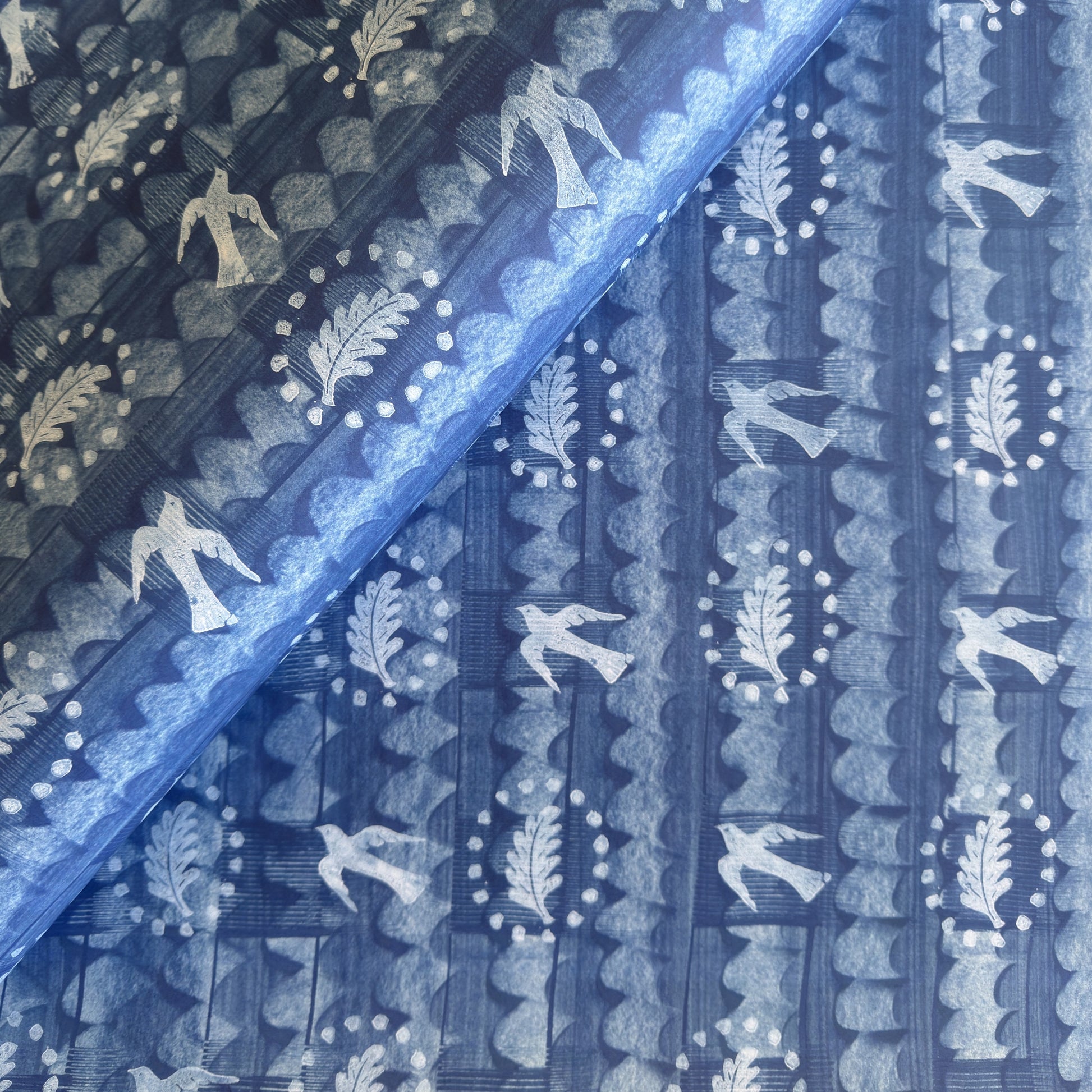 a sheet of wrapping paper with a relief printed oak leaf and bird in white on a blue paste paper backdrop