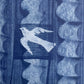 a sheet of wrapping paper with a relief printed oak leaf and bird in white on a blue paste paper backdrop