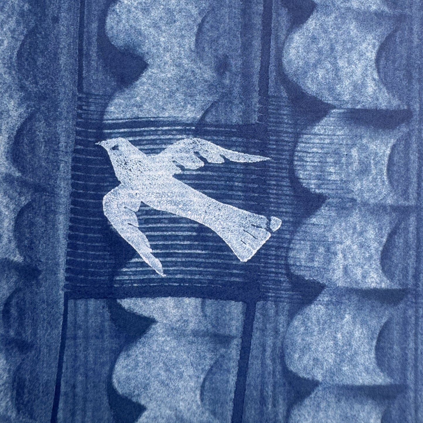 a sheet of wrapping paper with a relief printed oak leaf and bird in white on a blue paste paper backdrop