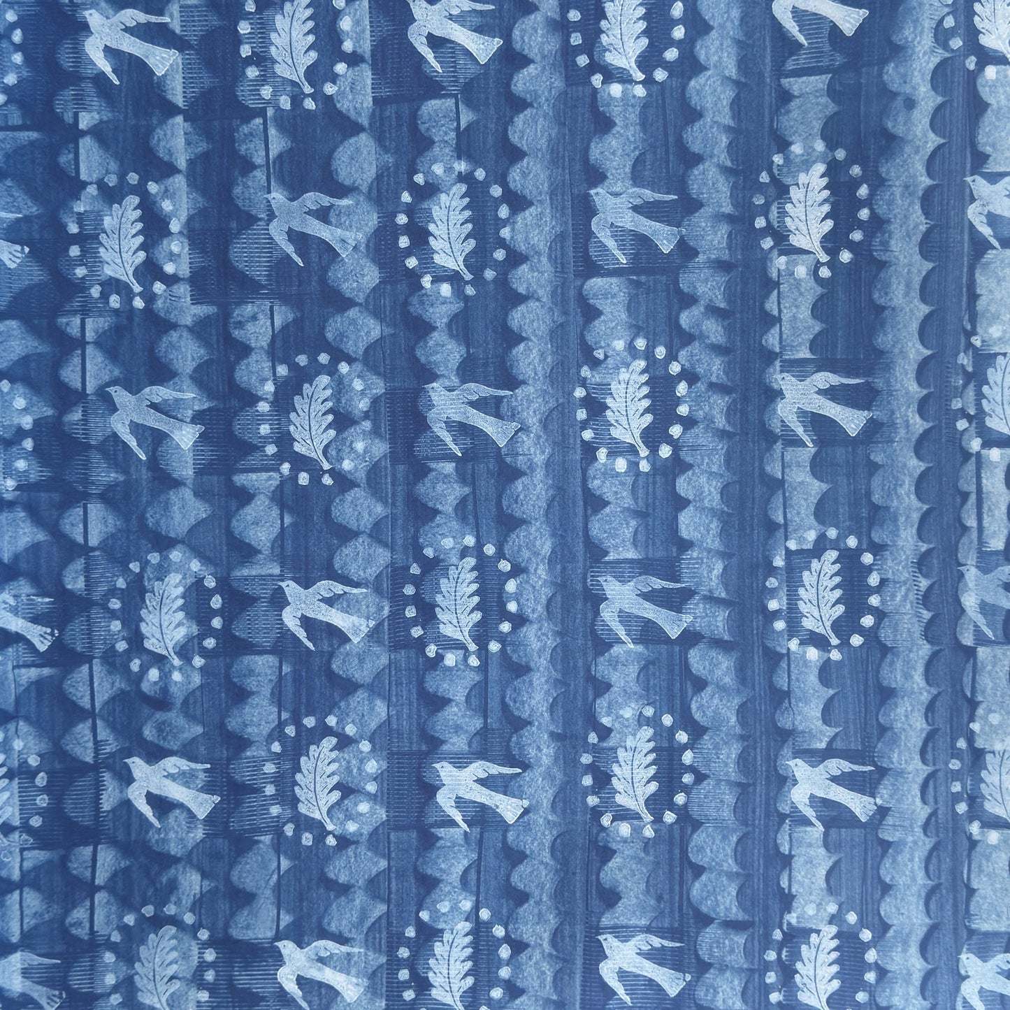a sheet of wrapping paper with a relief printed oak leaf and bird in white on a blue paste paper backdrop