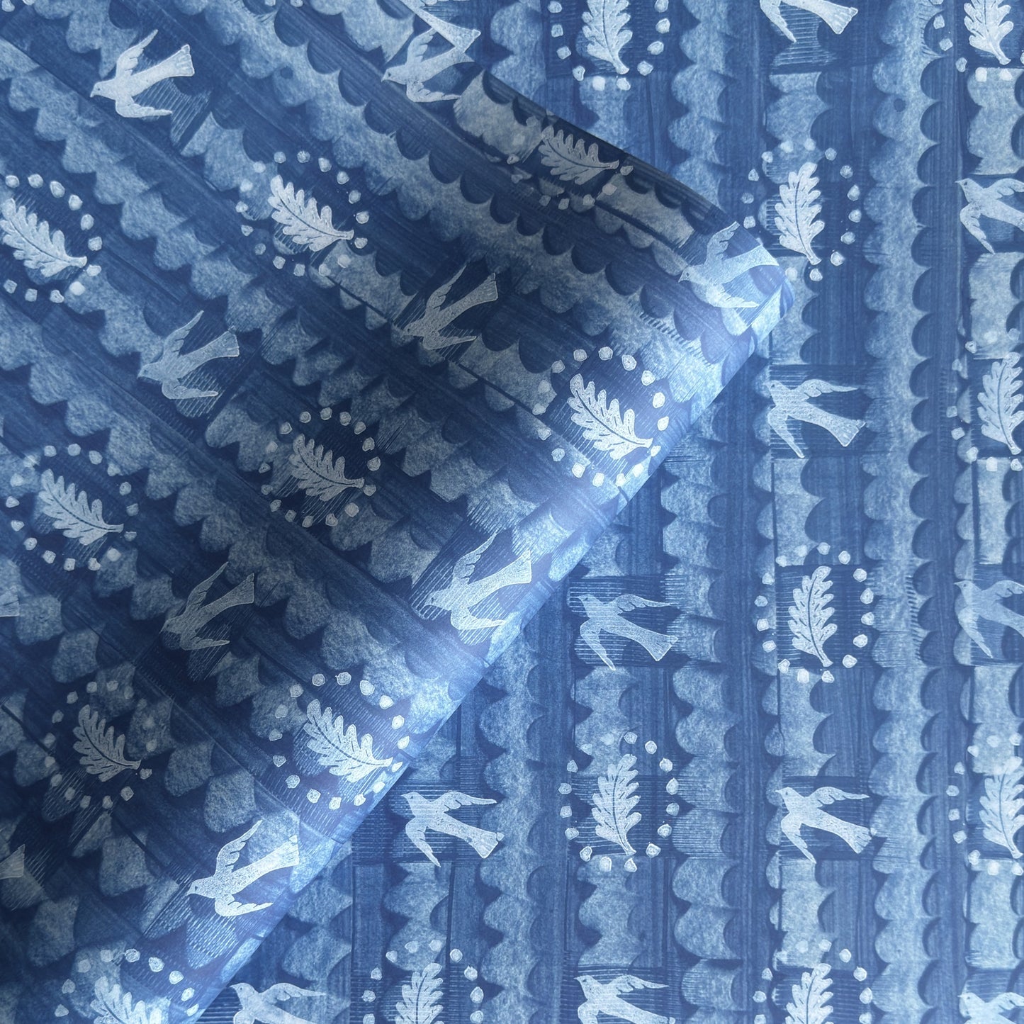a sheet of wrapping paper with a relief printed oak leaf and bird in white on a blue paste paper backdrop