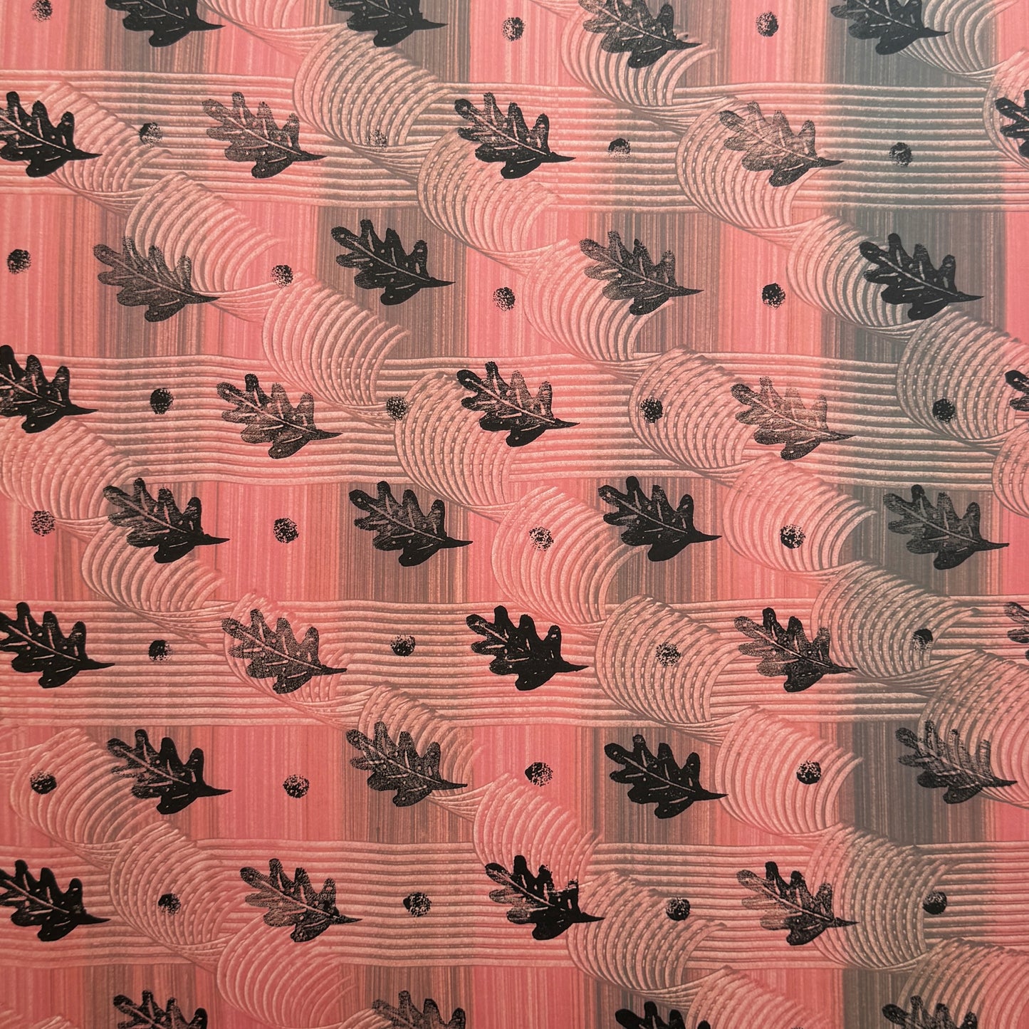  a sheet of wrapping paper with a relief printed black oak leaf on a coral pink paste paper backdrop