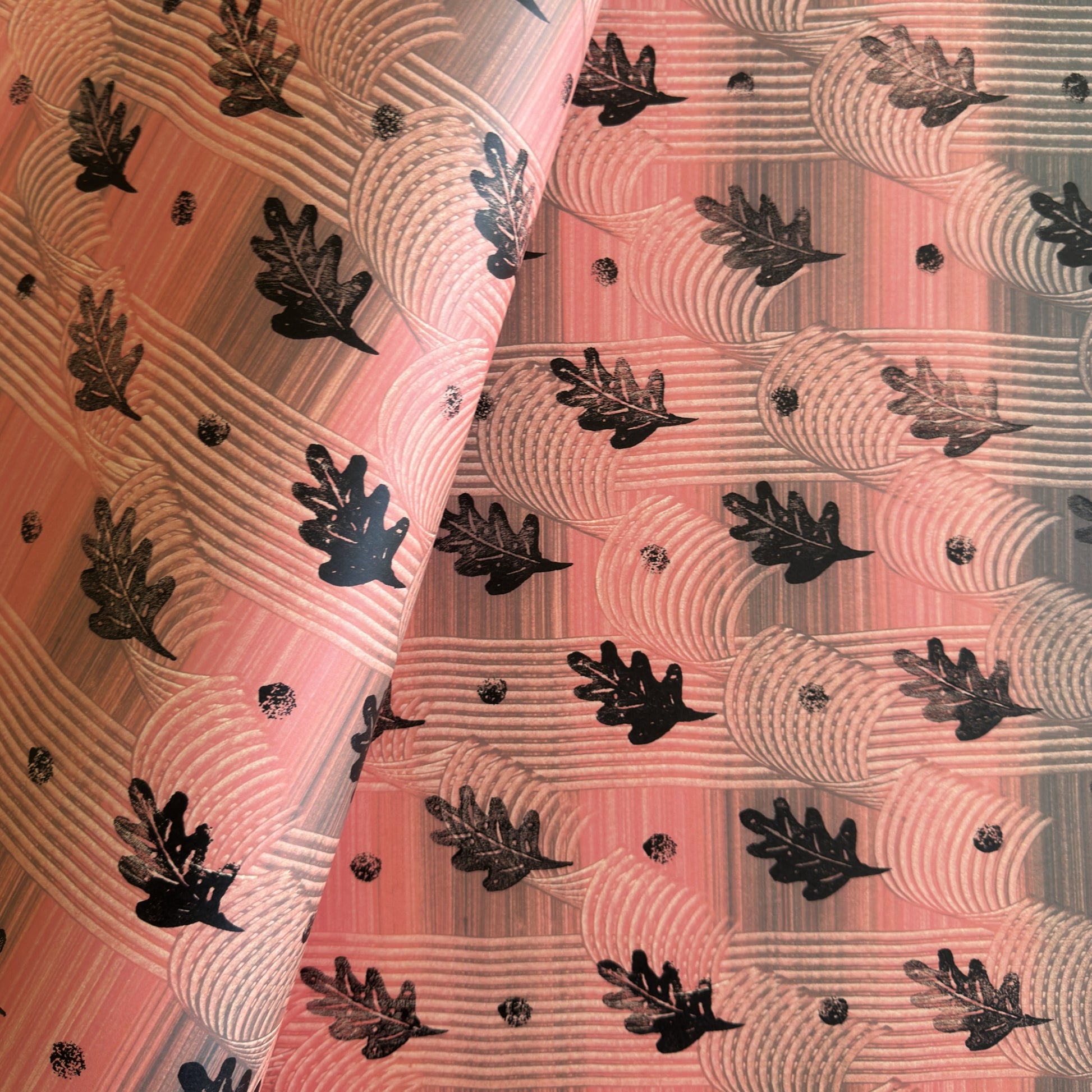  a sheet of wrapping paper with a relief printed black oak leaf on a coral pink paste paper backdrop
