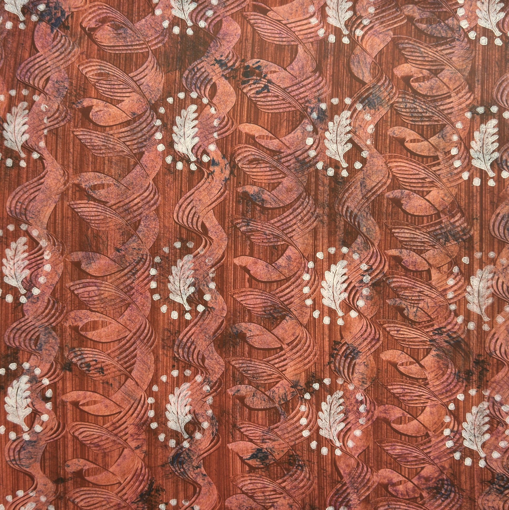 a sheet of wrapping paper with a relief printed oak leaf in white on a rust brown paste paper backdrop