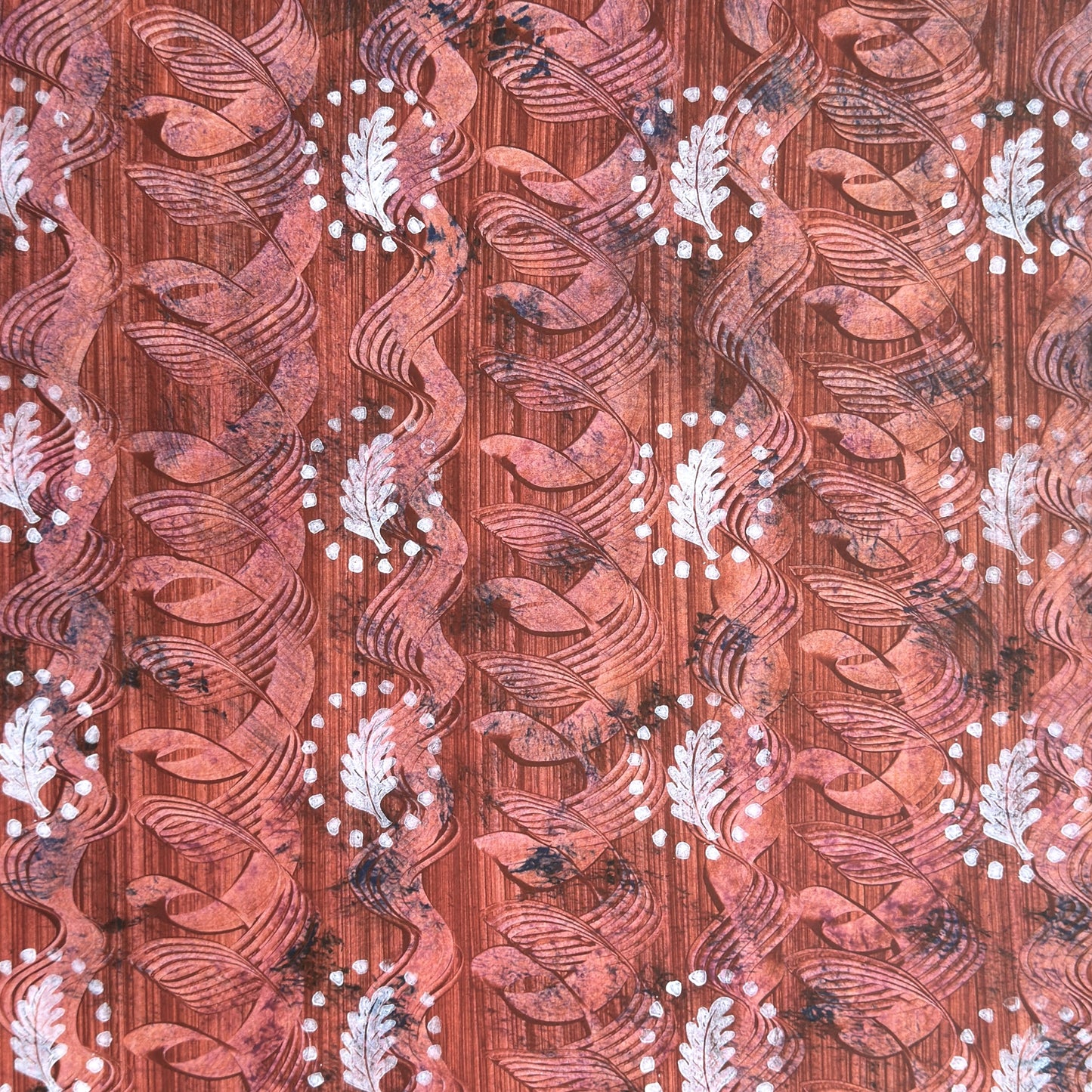 a sheet of wrapping paper with a relief printed oak leaf in white on a rust brown paste paper backdrop