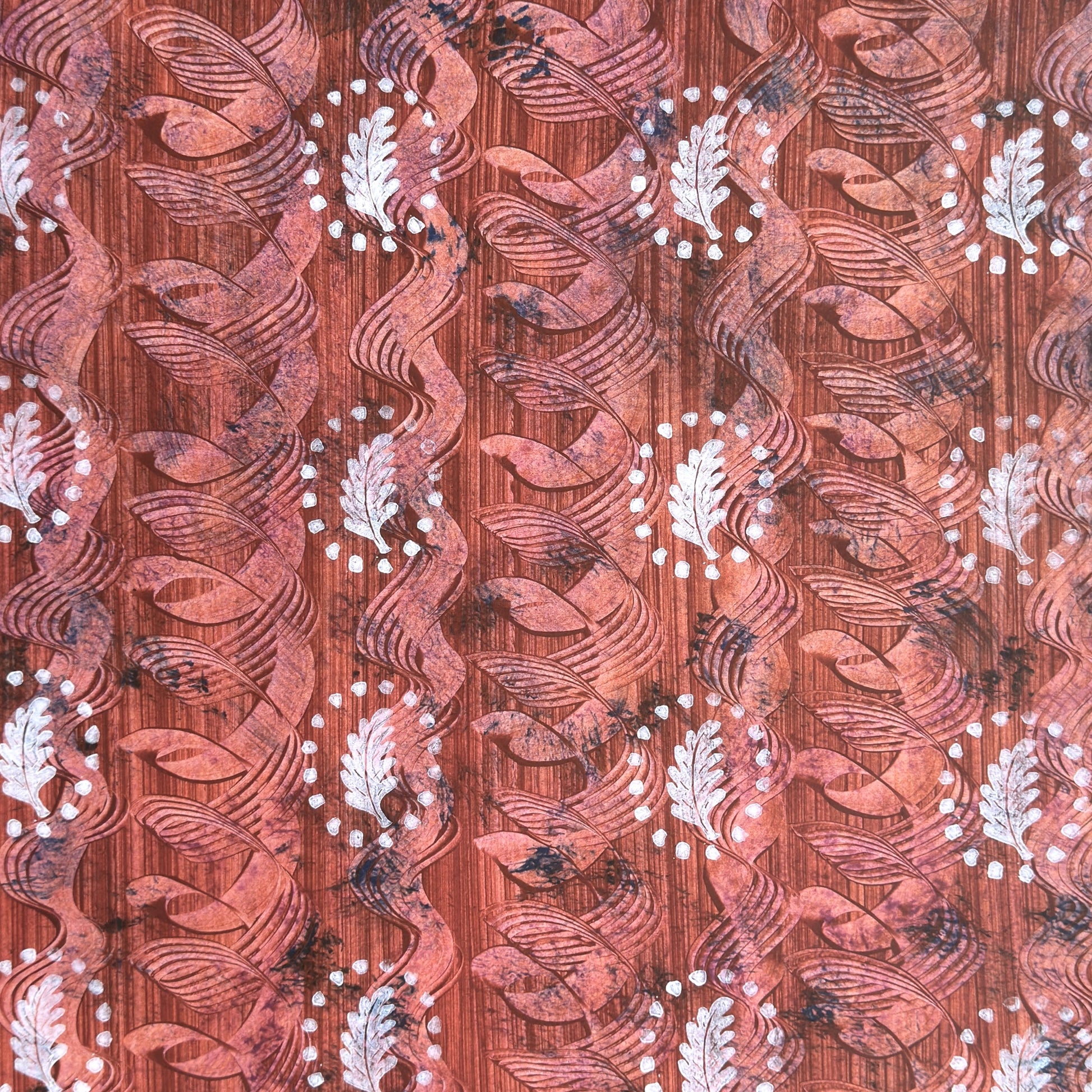 a sheet of wrapping paper with a relief printed oak leaf in white on a rust brown paste paper backdrop