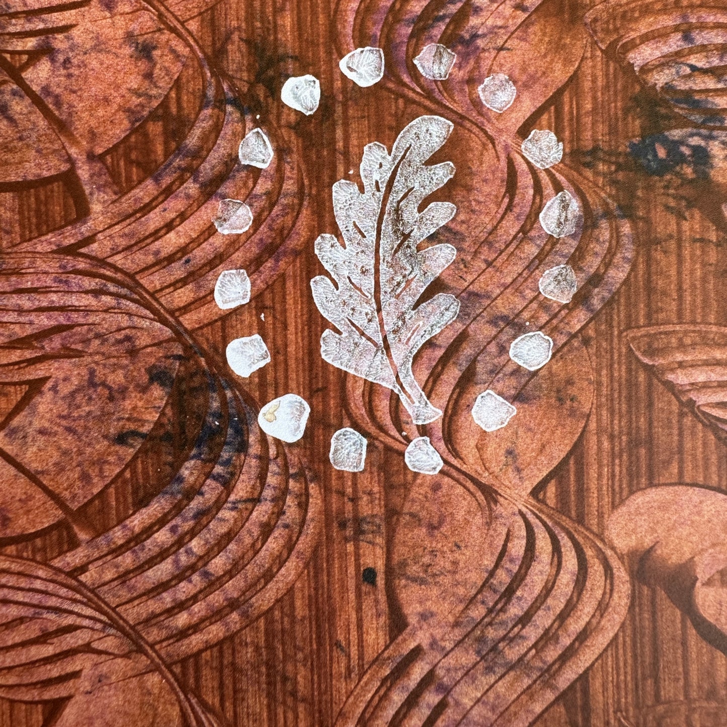 a sheet of wrapping paper with a relief printed oak leaf in white on a rust brown paste paper backdrop