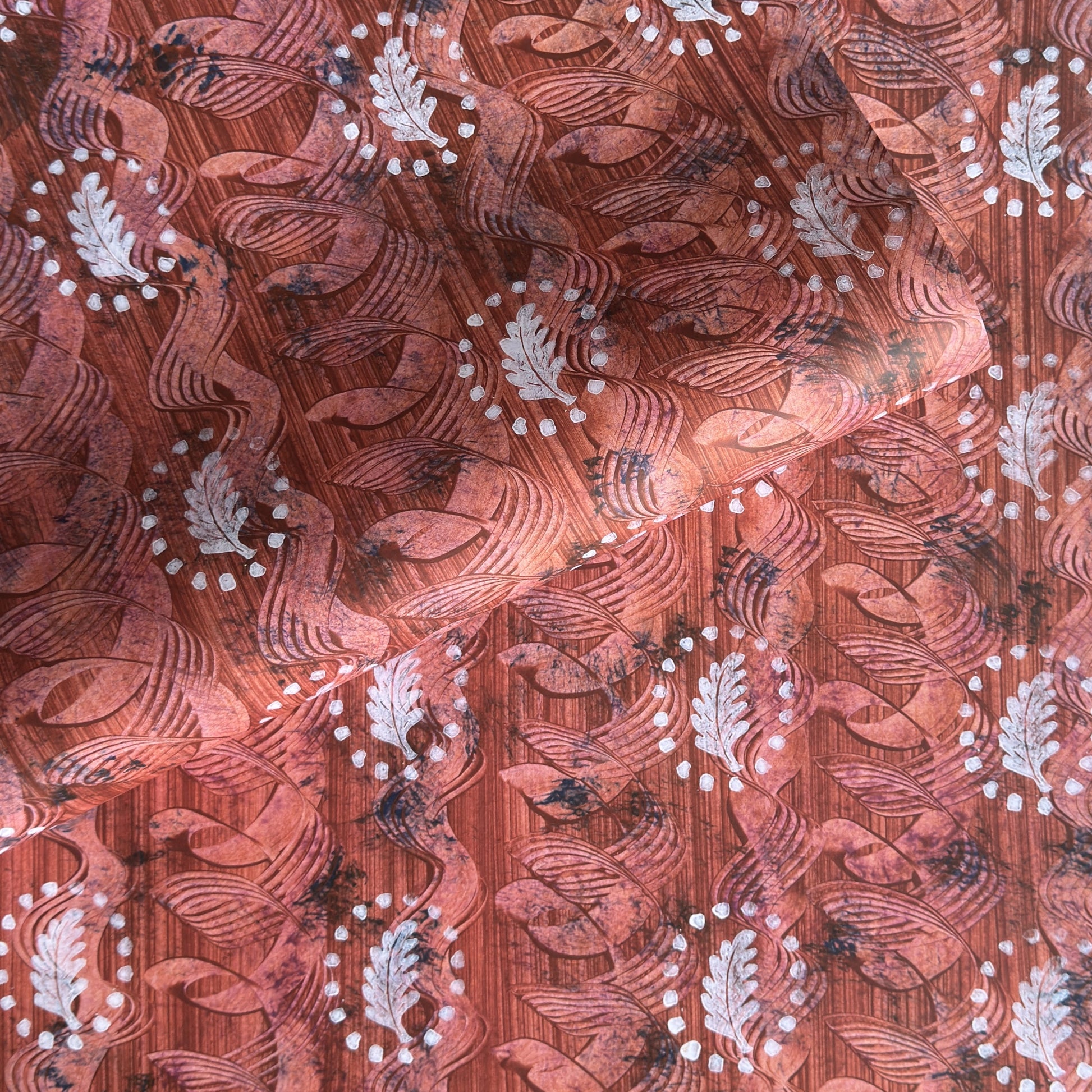 a sheet of wrapping paper with a relief printed oak leaf in white on a rust brown paste paper backdrop
