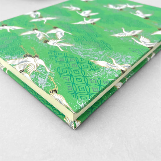 hardback A5 plain notebook with cover made of japanese silkscreen chiyogami paper. Large white cranes in flight on a green background by Esmie