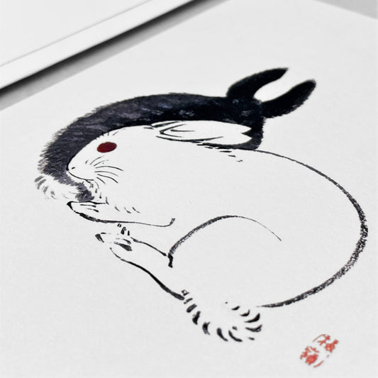 greetings card showing a drawing of one black rabbit and one white rabbit sitting together by Ezen Design