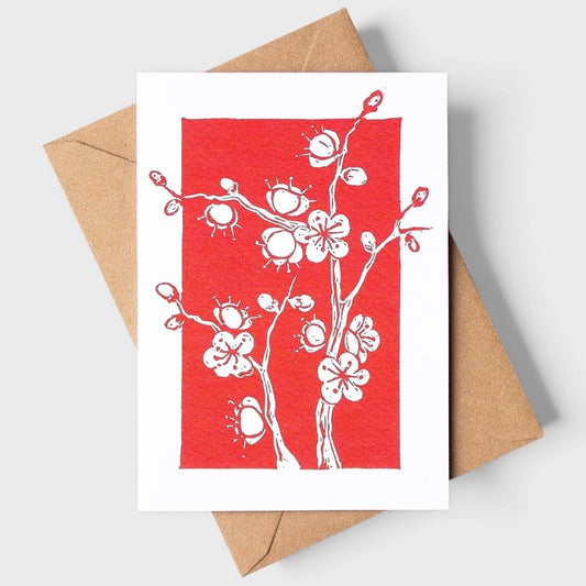 Greeting card with white floral plum blossom design on a red background, accompanied by a brown envelope.