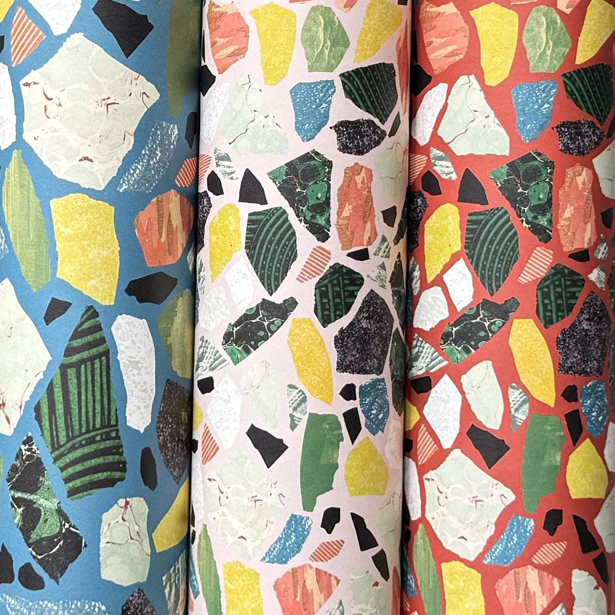 three rolls of wrapping paper with a terrazzo pattern in teal, pale pink and red
