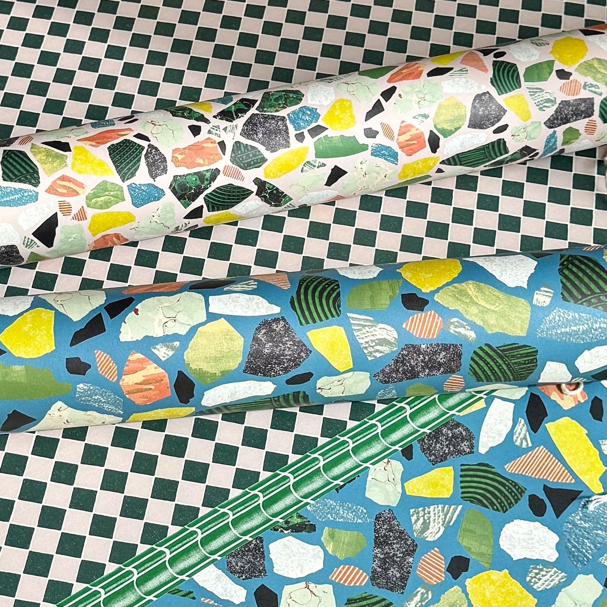 Colorful terrazzo pattern on a pale pink background. Rolled sheet of wrapping paper on a chequerboard backdrop