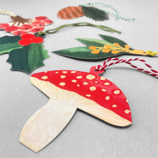 A set of five different festive plant gift tags in red, green and yellow with colourful sttring, by Hadley Paper Goods, pictured a red mushroom