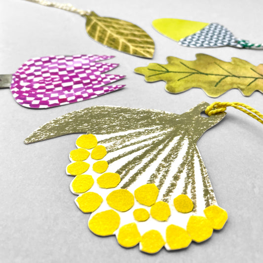 A set of five different plant shaped gift tags in colours of green, yellow and purple, with colourful string by Hadley Paper Goods, pictured a yellow flower head
