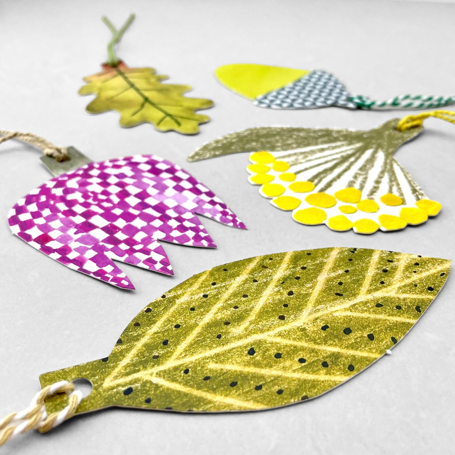 A set of five different plant shaped gift tags in colours of green, yellow and purple, with colourful string by Hadley Paper Goods, pictured a leaf
