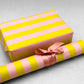wide classic stripe wrapping paper in lime green and dusty pink by Heather Evelyn. Pictured wrapped as a present with a roll of the patterned paper alongside