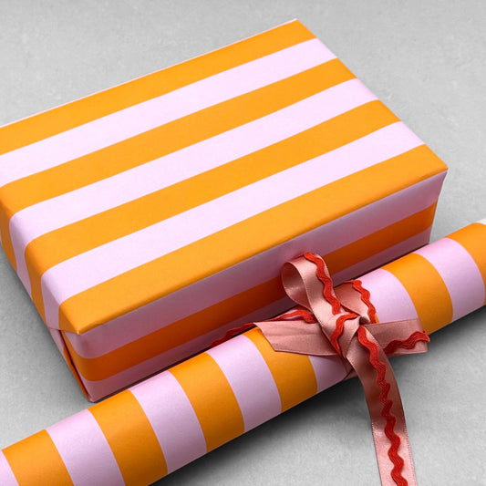 wide classic stripe wrapping paper in orange and pink by Heather Evelyn. Wrapped as a present with a roll of the patterned paper alongside