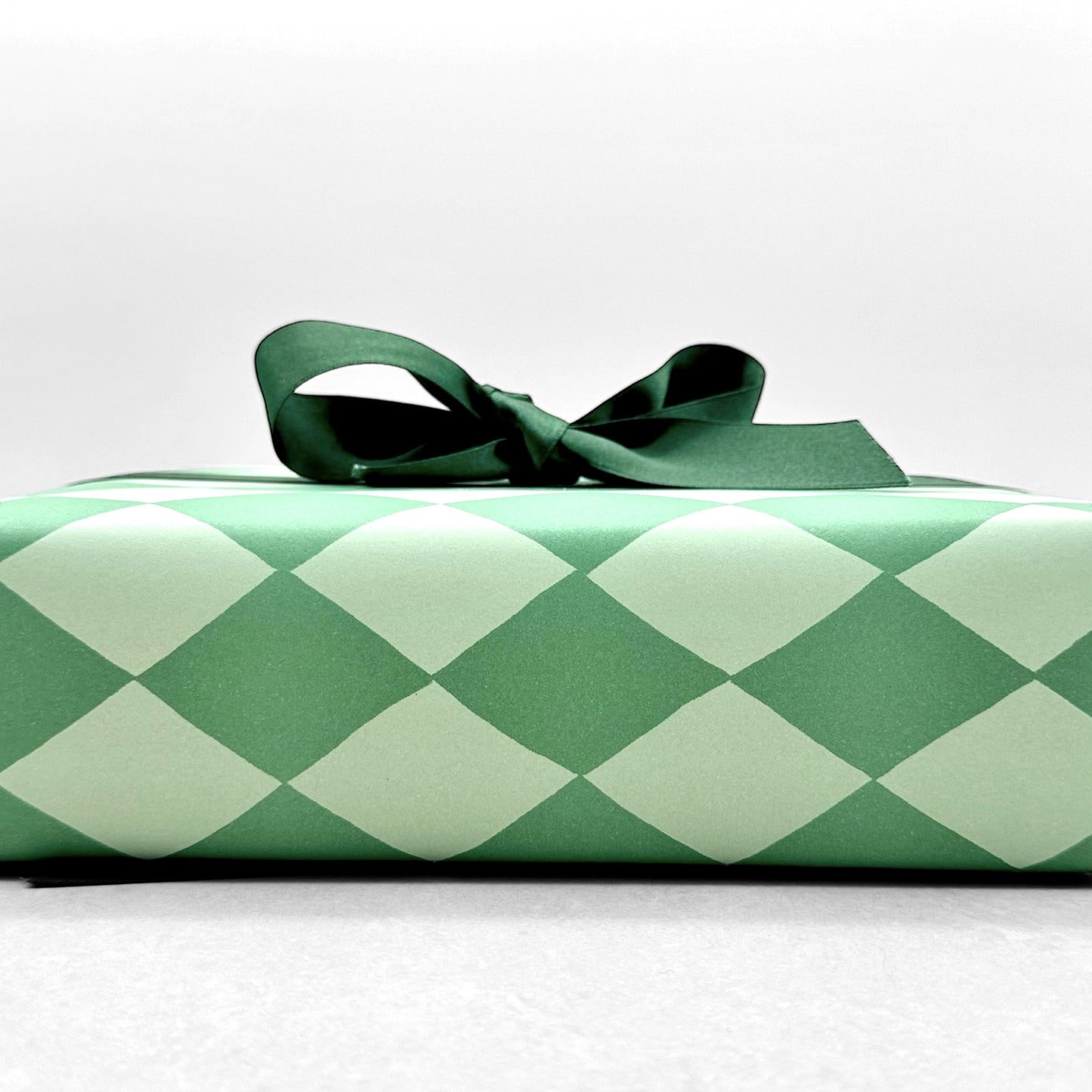 a sheet of wrapping paper with a two tone green large diamond pattern. By Heather Evelyn and shown wrapped as a gift with a green satin bow