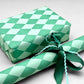 a sheet of wrapping paper with a two tone green large diamond pattern. By Heather Evelyn and shown wrapped as a gift