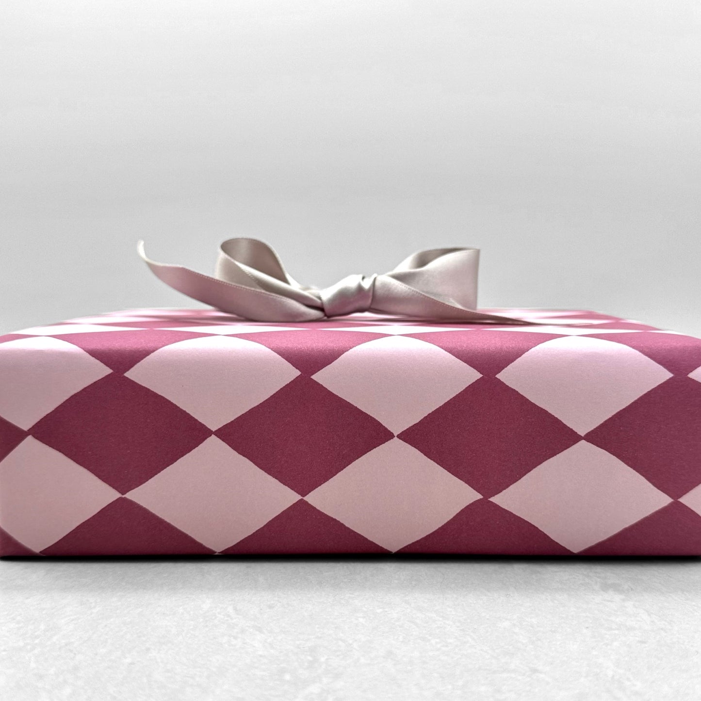 wrapping paper with large diamond design in mauve and pink. Pictured wrapped as a present with a silver bow