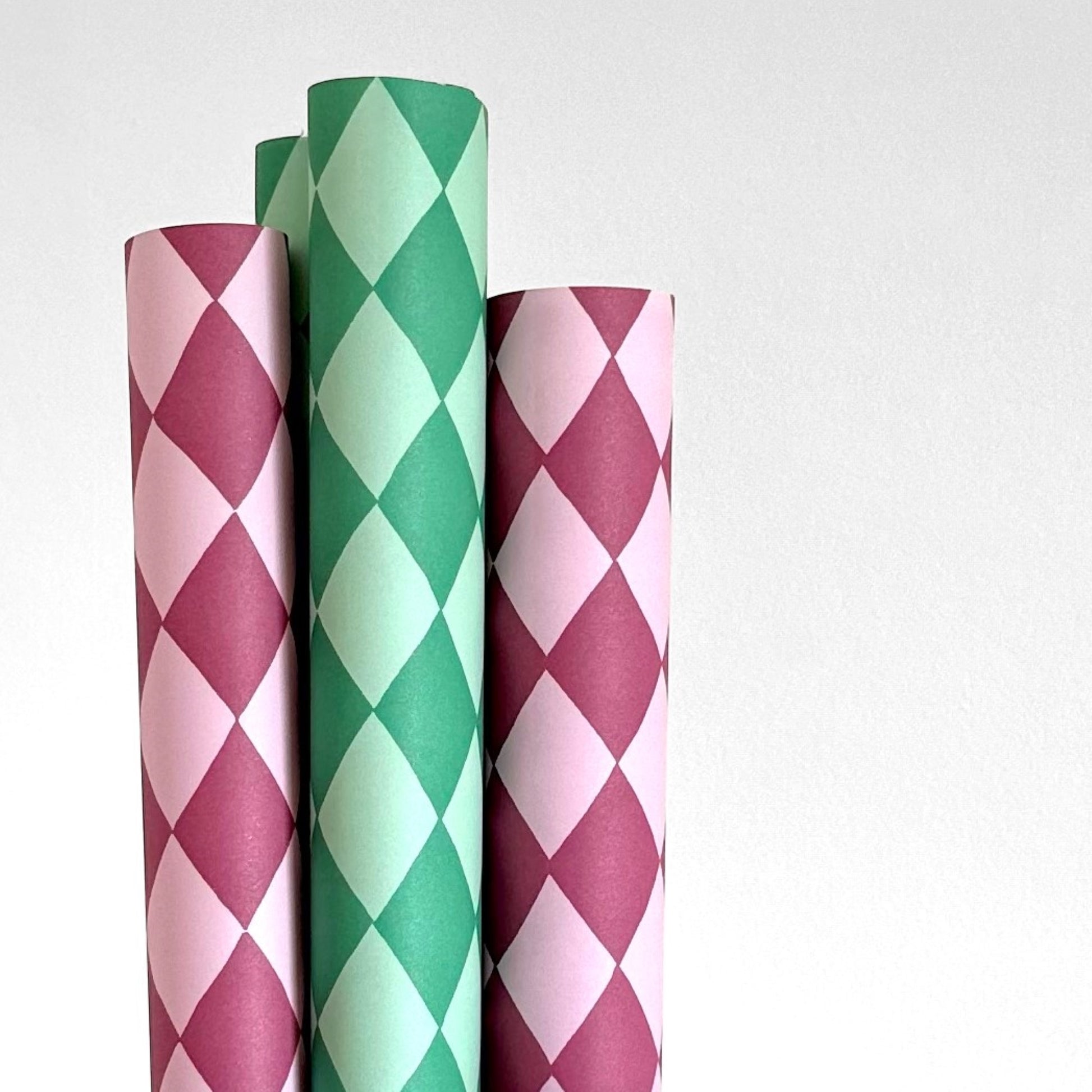 wrapping paper with large diamond design in mauve and pink. Pictured rolled alongside a green version of the wrap