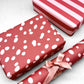 burgundy rouge wrapping paper with random blush pink spots, by Heather Evelyn. Pictured wrapped alongside a striped red and pink present.