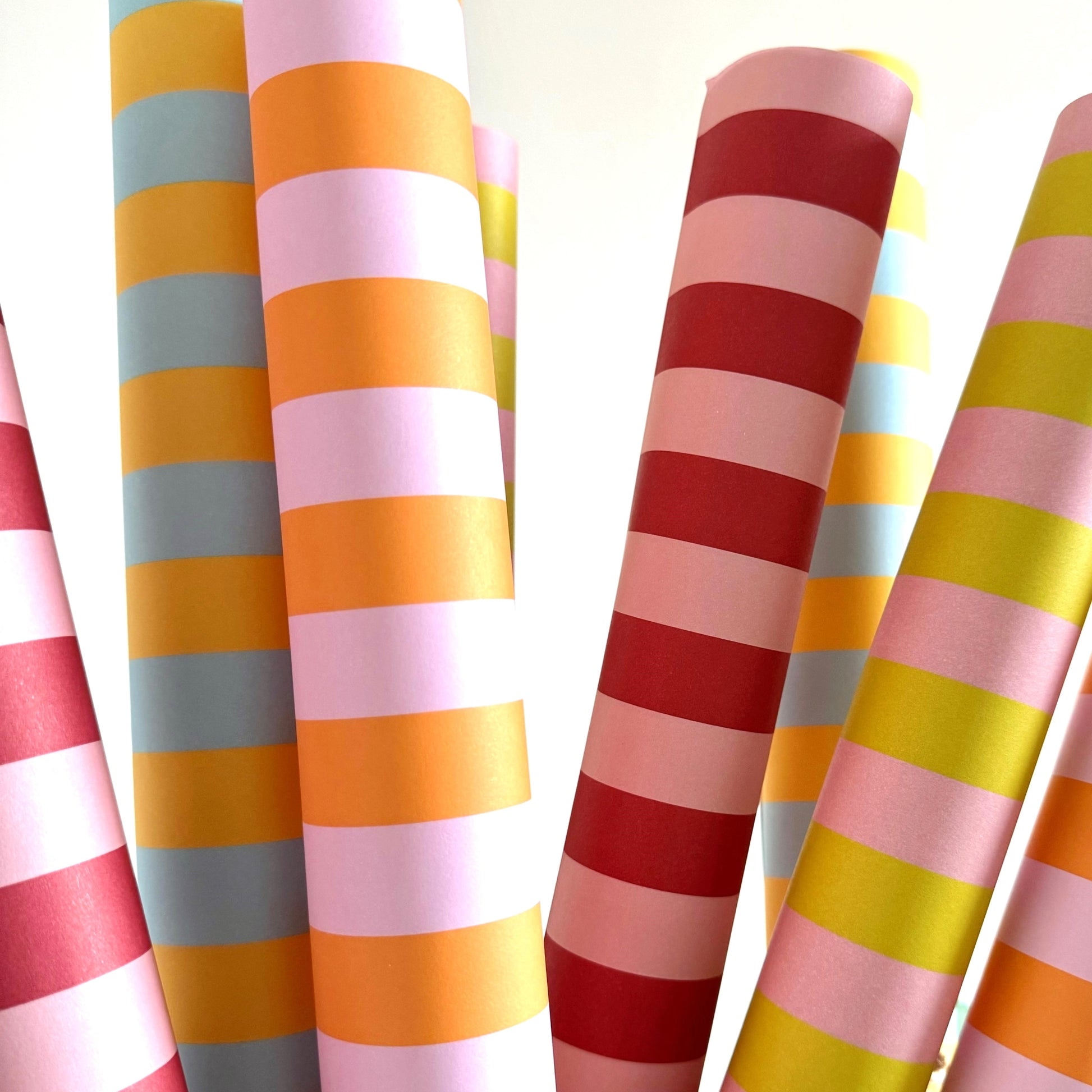 wide classic stripe wrapping paper in red and pink by Heather Evelyn. Pictured rolled with other striped patterned papers