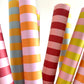 wide classic stripe wrapping paper in orange and pink by Heather Evelyn. Pictured rolled with other striped designs