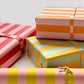 wide classic stripe wrapping paper in lime green and dusty pink by Heather Evelyn. Pictured rolled in front of presents wrapped in other colour stripes