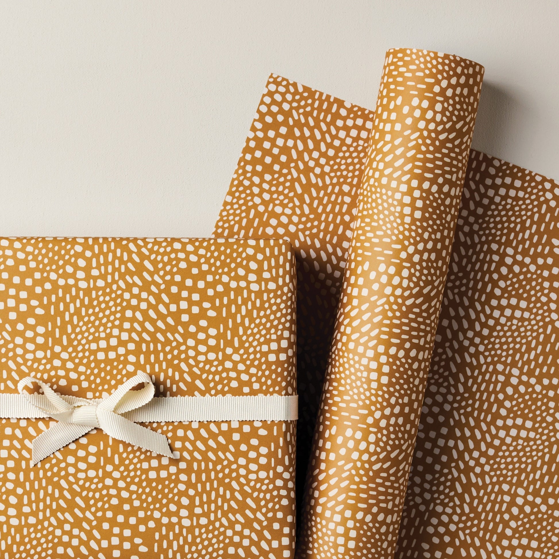 a sheet of wrapping paper in mustard with a small abstract pattern in white