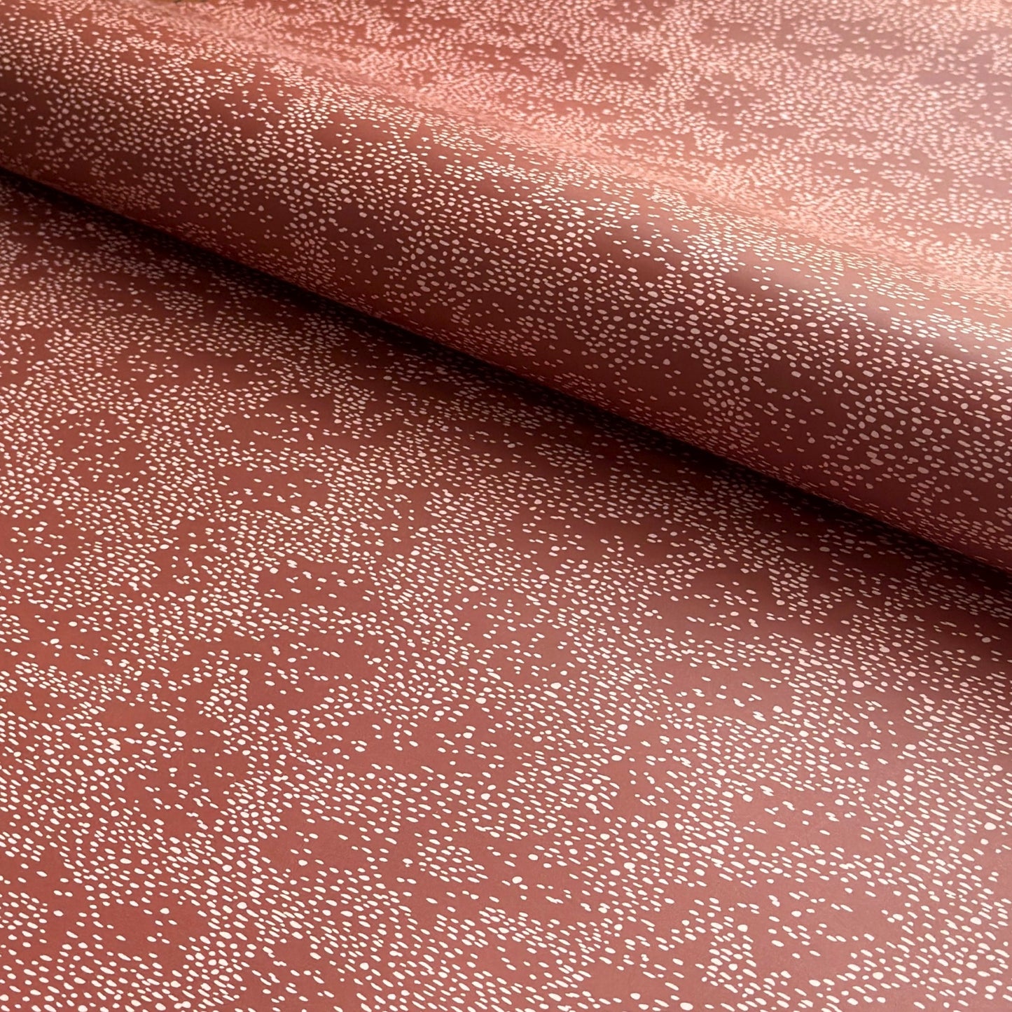 a sheet of wrapping paper in rust with an abstract pink speckled design