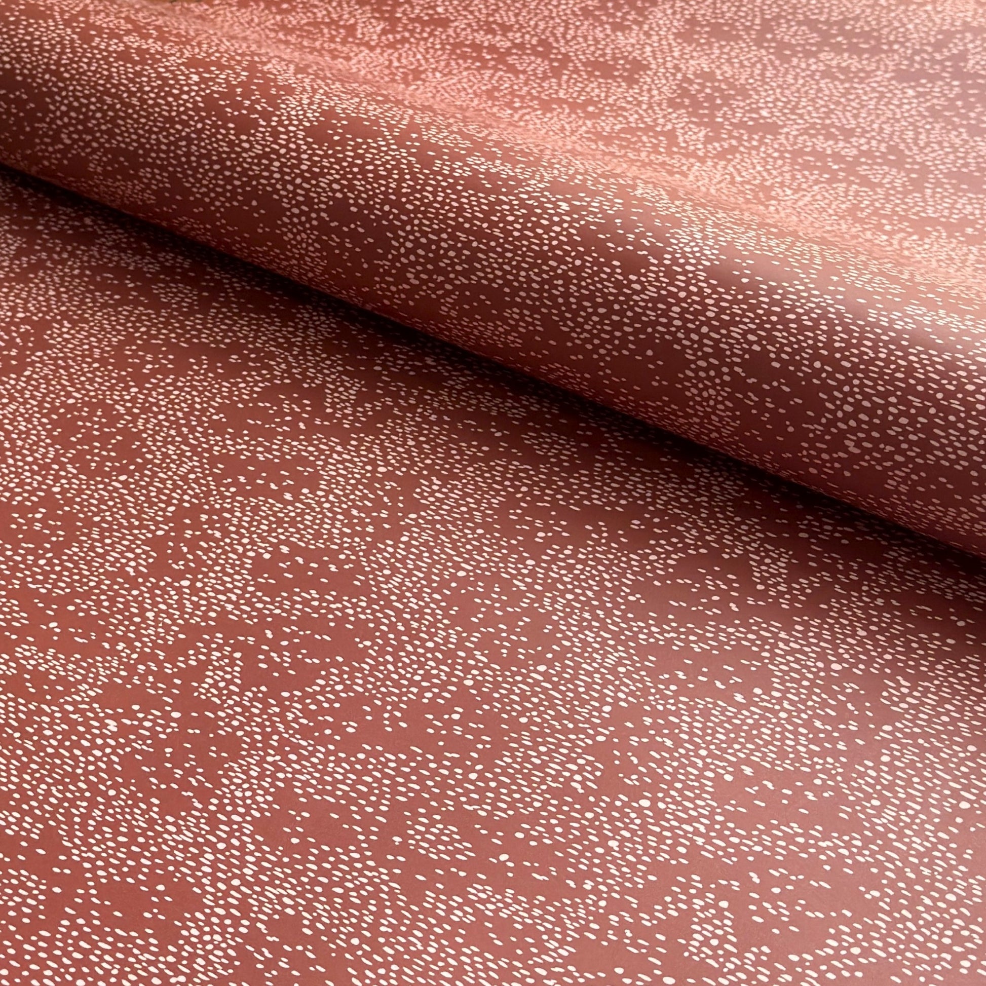 a sheet of wrapping paper in rust with an abstract pink speckled design