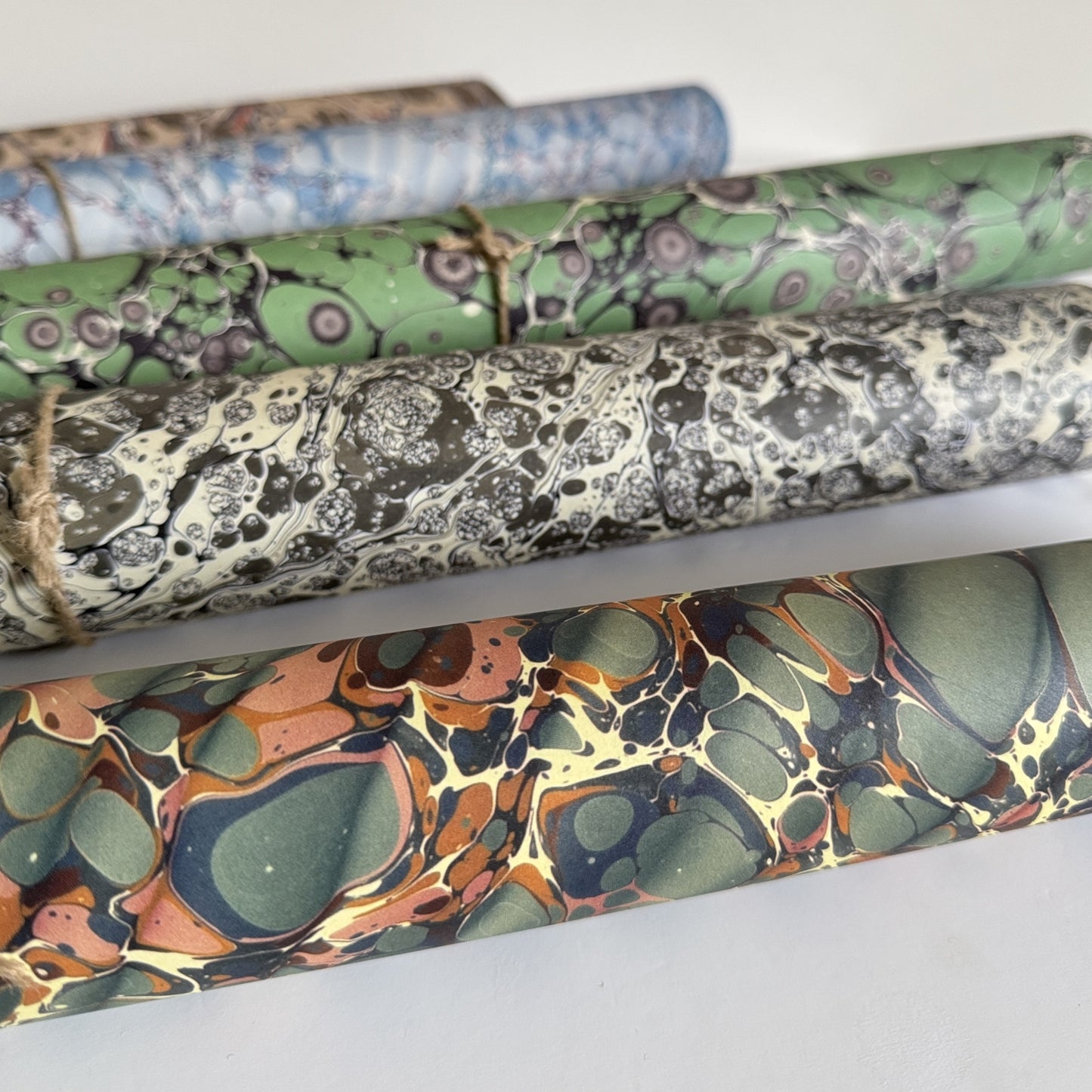 sheet of printed marbled wrapping paper by Jemma Lewis, ripple effect in teal green, ochre and pink. Pictured rolled