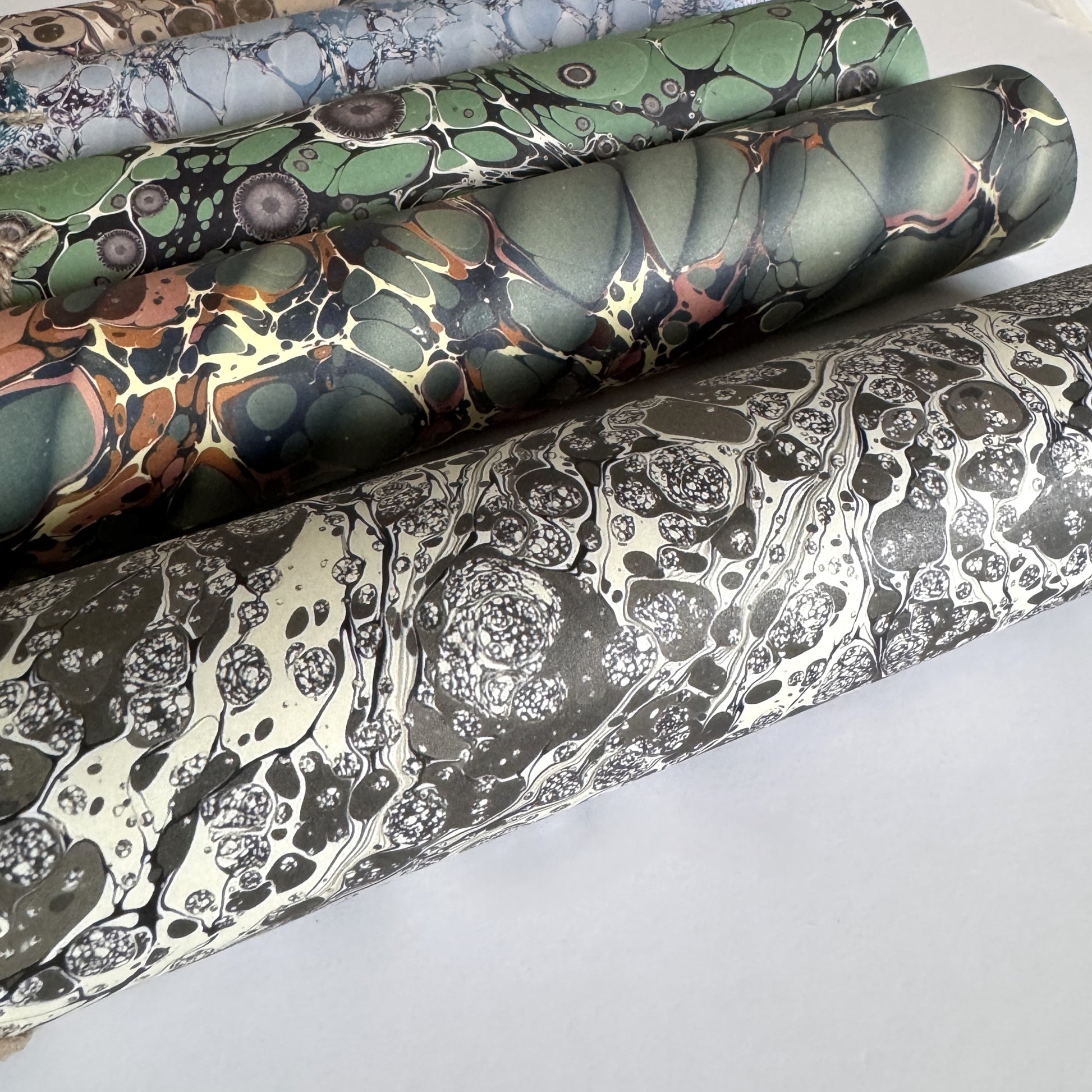 sheet of printed marbled wrapping paper by Jemma Lewis, stone effect in taupe, black and beige. Pictured rolled
