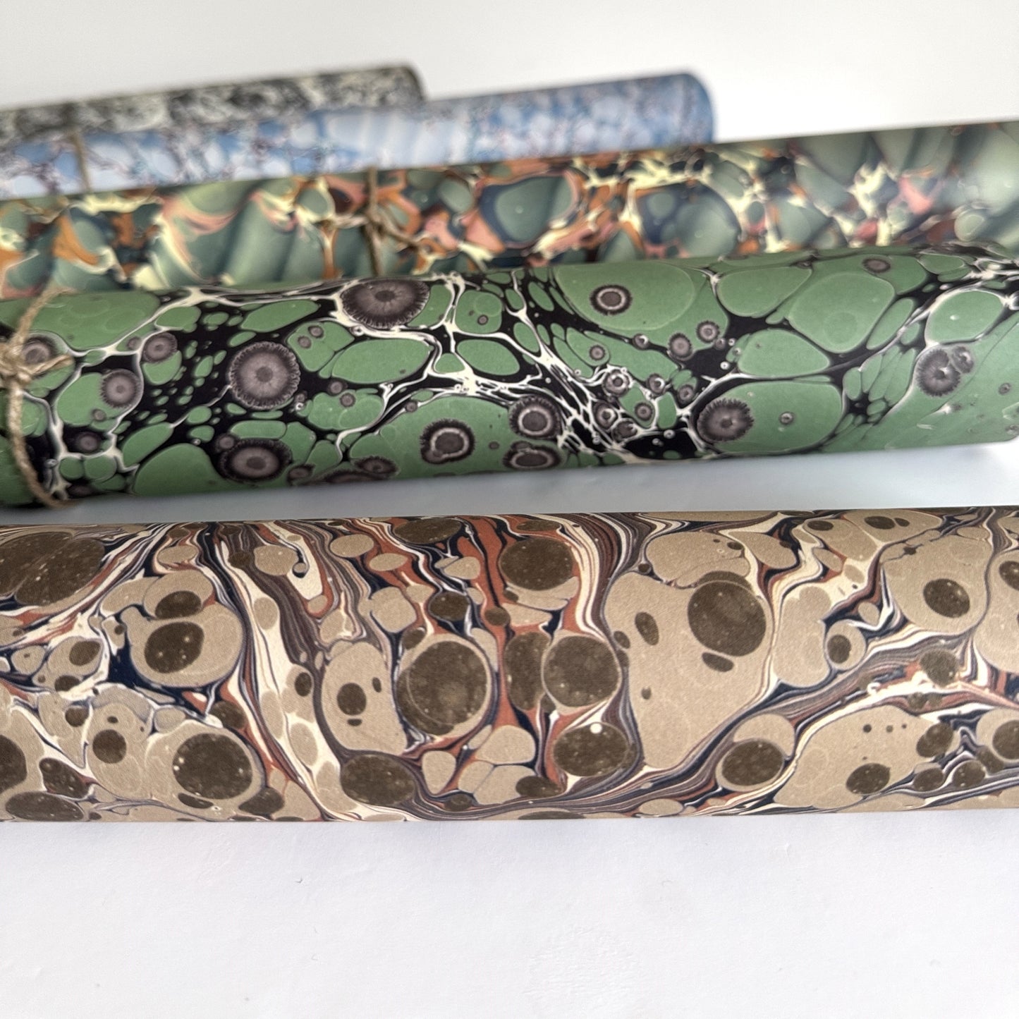 sheet of printed marbled wrapping paper by Jemma Lewis, stone effect in taupe, blush pink and beige. Pictured rolled