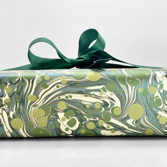 Printed marbled wrapping paper by Jemma Lewis Marbling. Marbled paper with a shimmery base paper and marbled pattern in green, lime and white. Pictured wrapped with a green bow