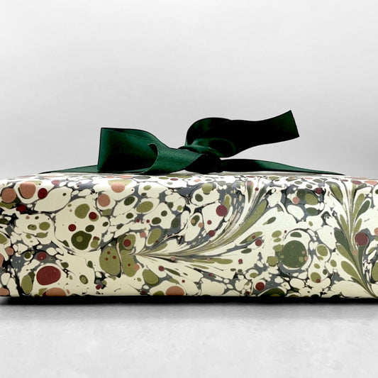 Printed marbled wrapping paper by Jemma Lewis Marbling. Marbled paper with a shimmery base paper and marbled pattern in burgundy, green and white. Pictured wrapped with a green bow