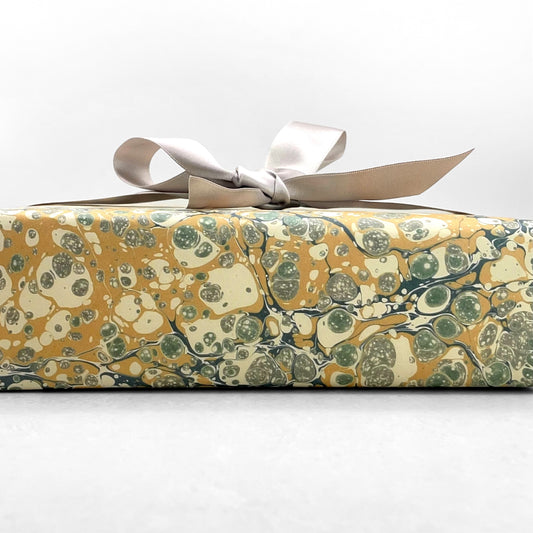 Printed marbled wrapping paper by Jemma Lewis Marbling. Marbled paper in soft greens, teal and yellow. Pictured wrapped with a bow